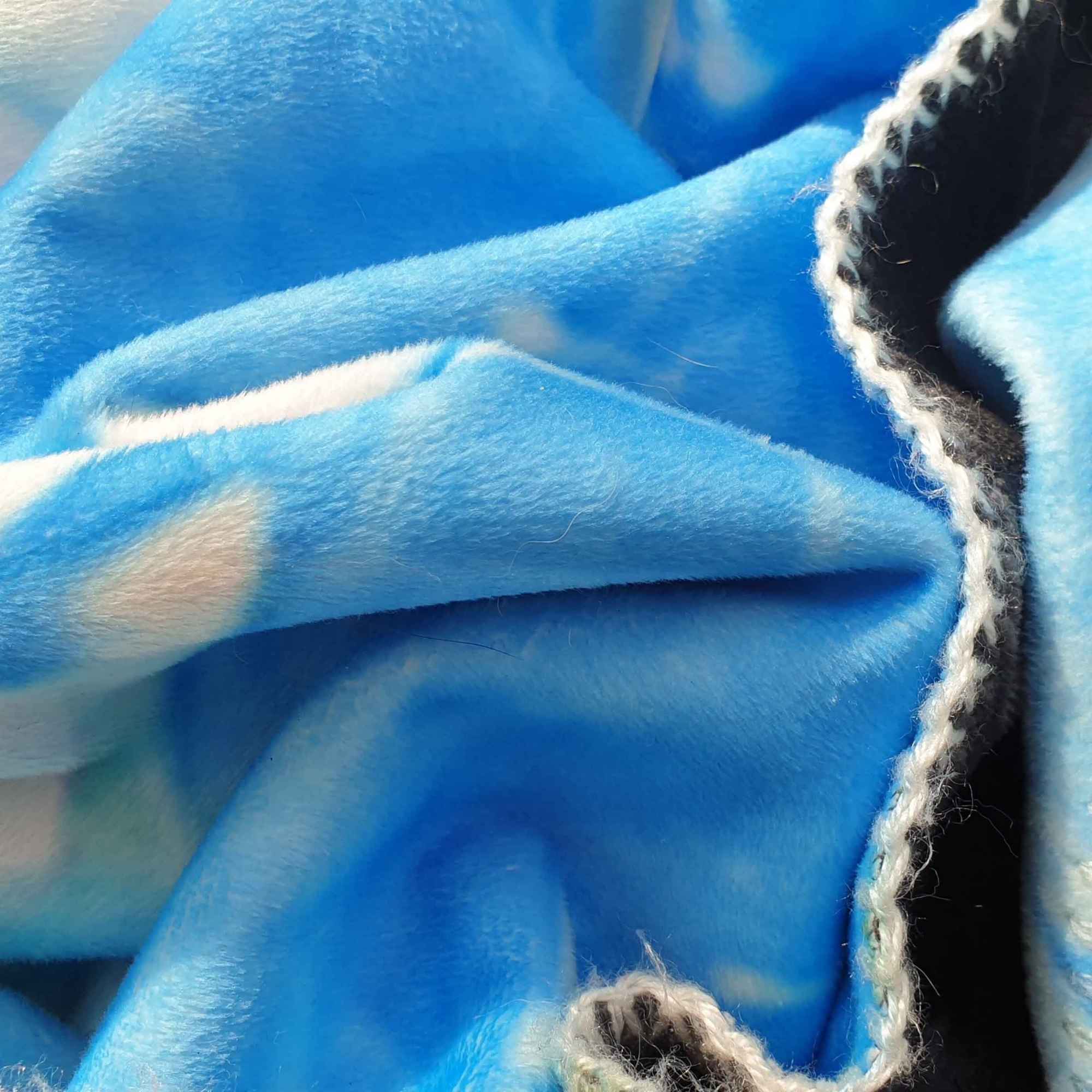 Nahaufnahme einer himmelblauen Kuscheldecke mit weißen Wolkenmustern und heller Kettelnaht.