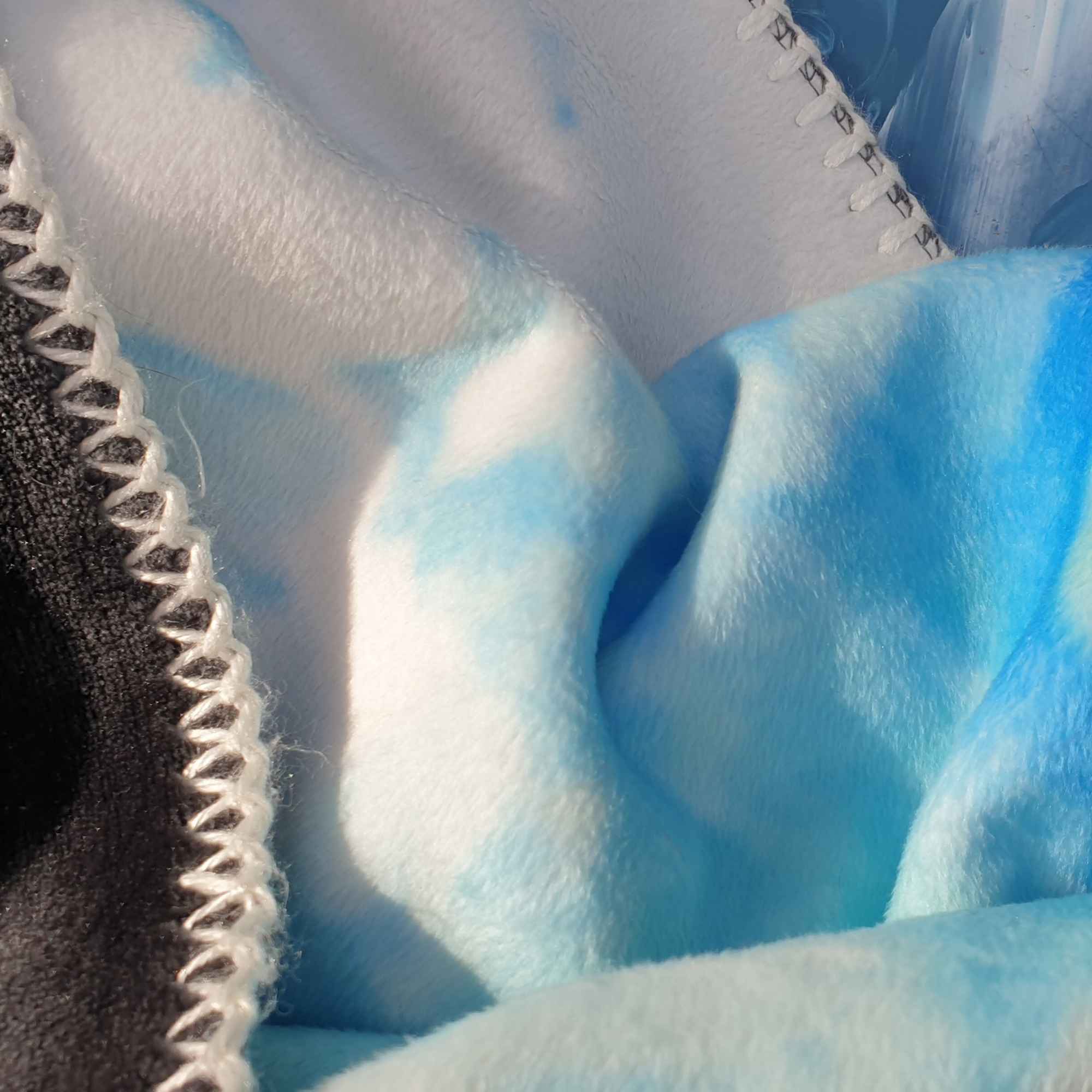 Detailansicht einer flauschigen Kuscheldecke in Himmelblau und Weiß mit heller Ziernaht.