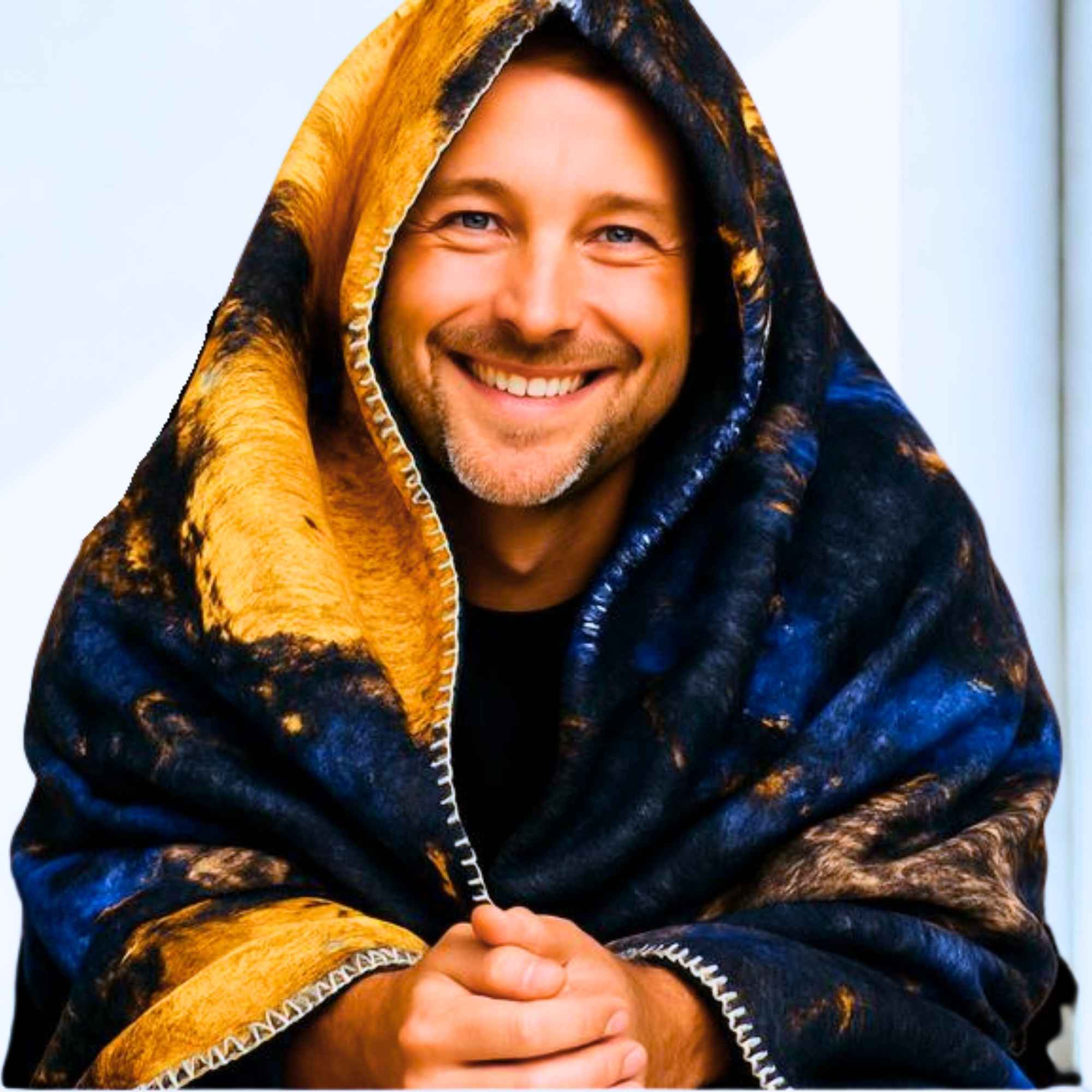 Lächelnder Mann, in eine flauschige Kuscheldecke mit dunklem Muster und goldenen Akzenten gehüllt.