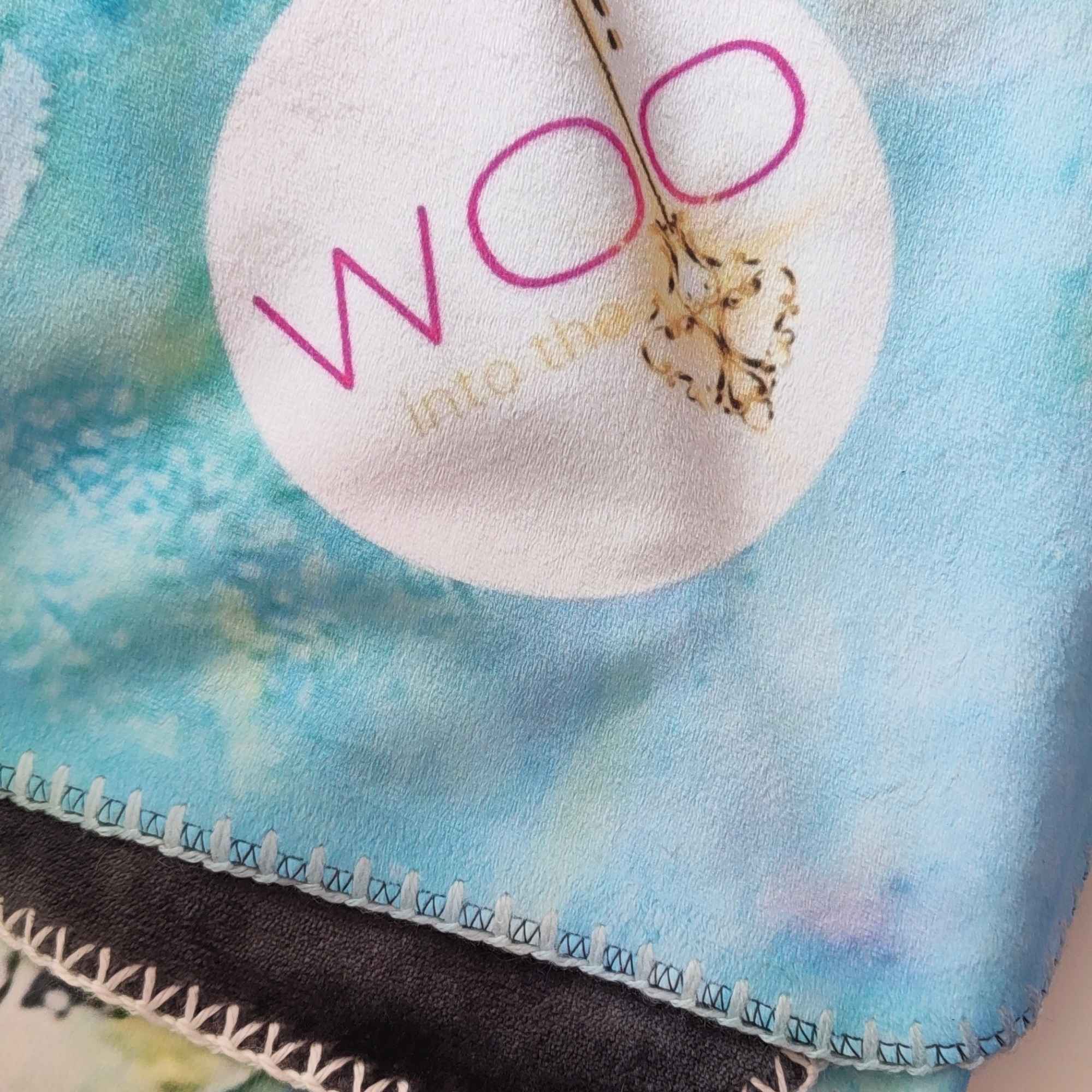 Nahaufnahme der flauschigen Kuscheldecke FORREST GUMP mit abstraktem Muster in Türkis, Weiß und Gelb sowie WOO-Label.