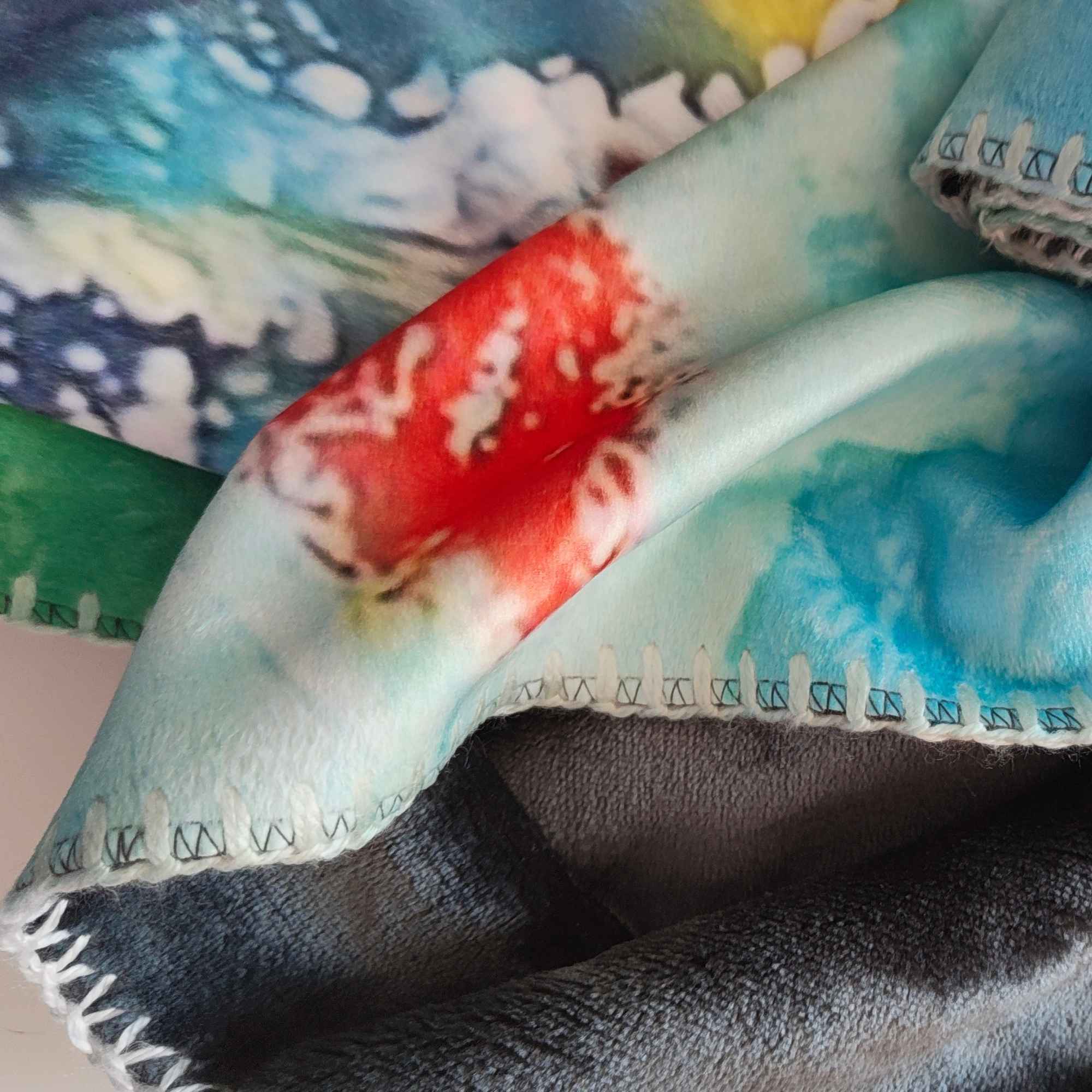 Gefaltete flauschige Kuscheldecke mit abstraktem Muster in Türkis, Blau, Rot, Weiß und Gelb sowie dekorativer Ziernaht - FORREST GUMP.