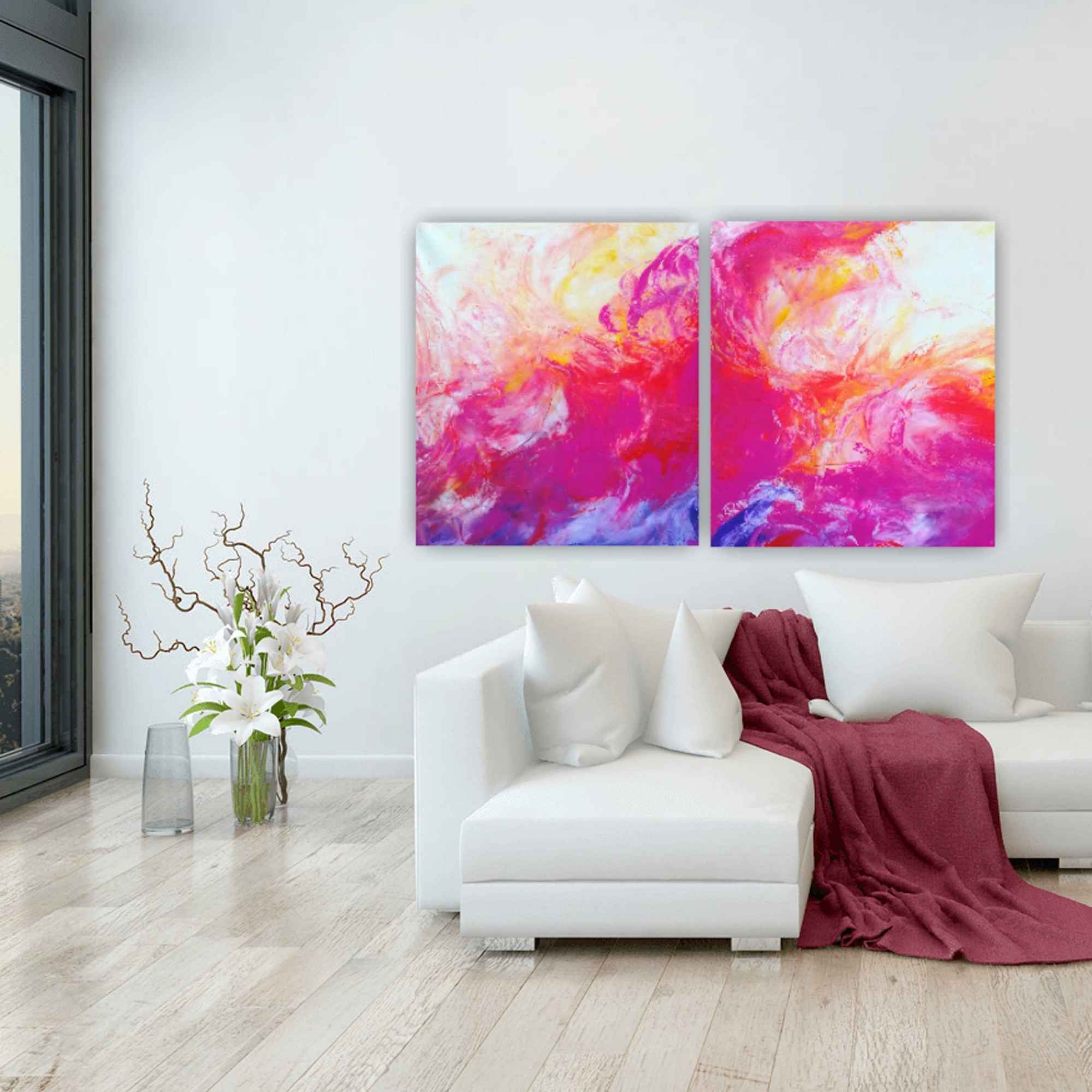 Zweiteiliges abstraktes Gemälde in leuchtenden Pink-, Orange- und Gelbtönen über einem weißen Sofa. Die Farben fließen über beide Leinwände hinweg und spiegeln sich in der Dekoration des Raums.