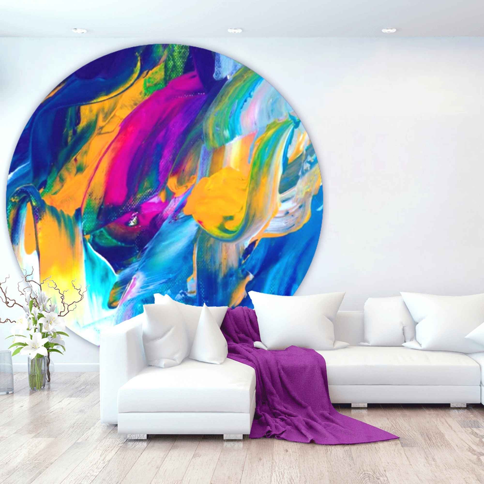 Runder, farbenfroher Teppich mit abstraktem Druck in Blau, Gelb, Pink und Grün vor einer weißen Sofalandschaft in modernem Wohnzimmer.