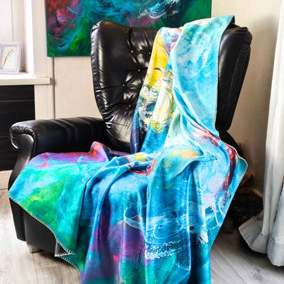 FORREST GUMP Kuscheldecke mit abstrakter Kunst - farbenfrohe Kunstdecke in Türkis, Blau, Grün und Pink auf einem schwarzen Ledersessel. Künstlerische Kuscheldecke nach dem Originalgemälde von MYSTIQUE, erhältlich bei INTO THE WOO.