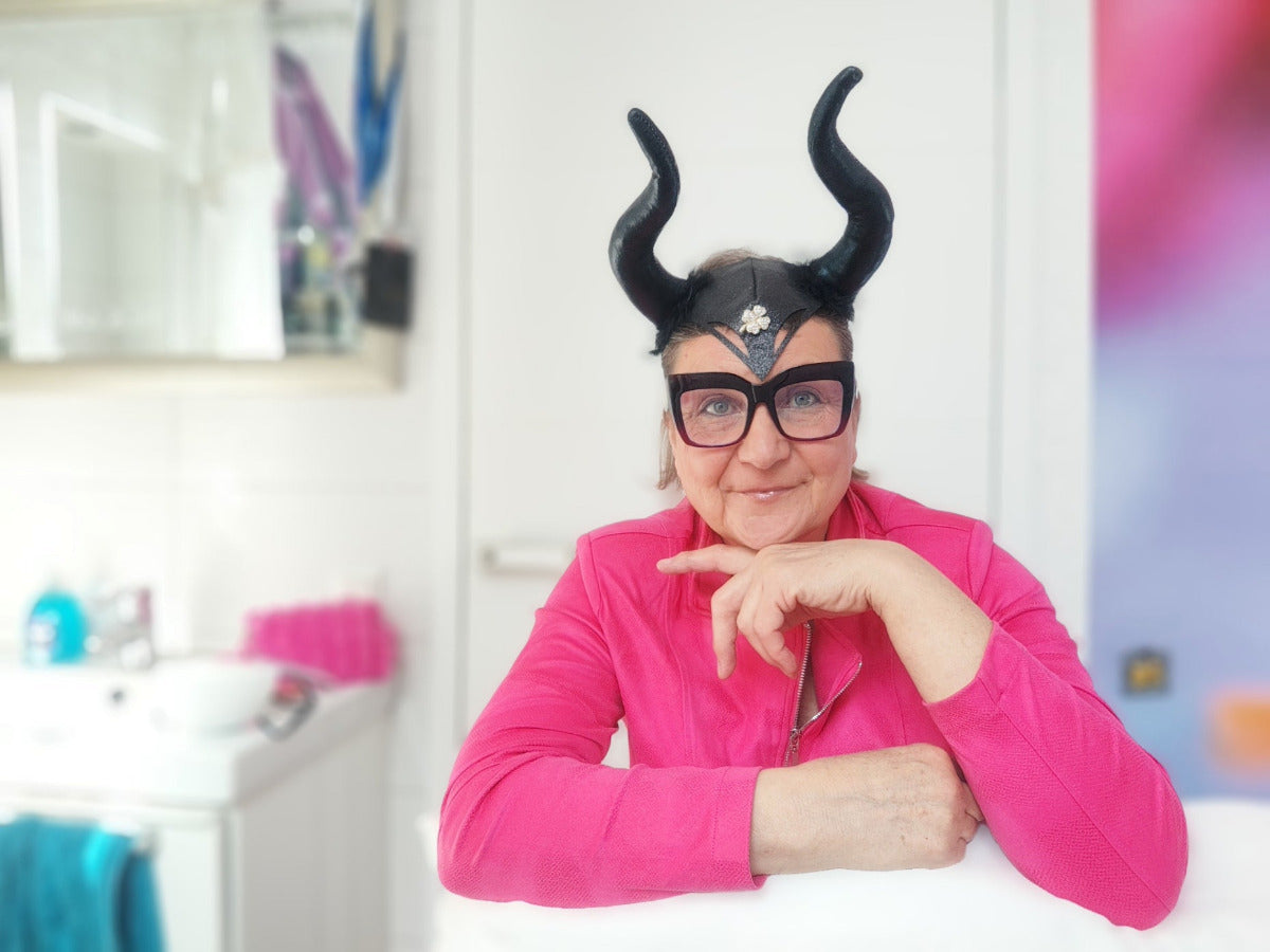 Grinsende Mystic Maveress mit Designerbrille, schwarzen Herrscherinnen-Hörnern und pinkfarbenem Oberteil
