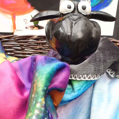 „Bunte Kuscheldecke mit plüschiger Oberfläche, präsentiert von einer schwarzen Schaf-Figur in einem Korb.“