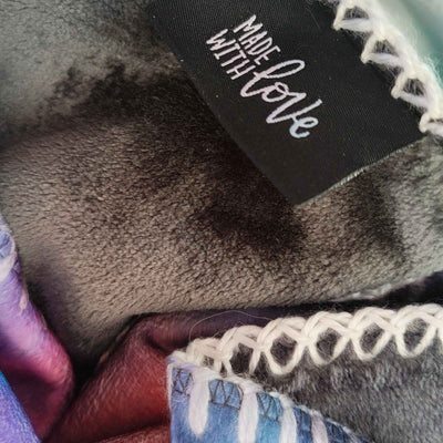 Detail einer weichen Kuscheldecke mit „Made with LOVE“-Label, dekorativer Ziernaht und abstraktem Motiv in Blau, Rot und Violett - FORREST GUMP.