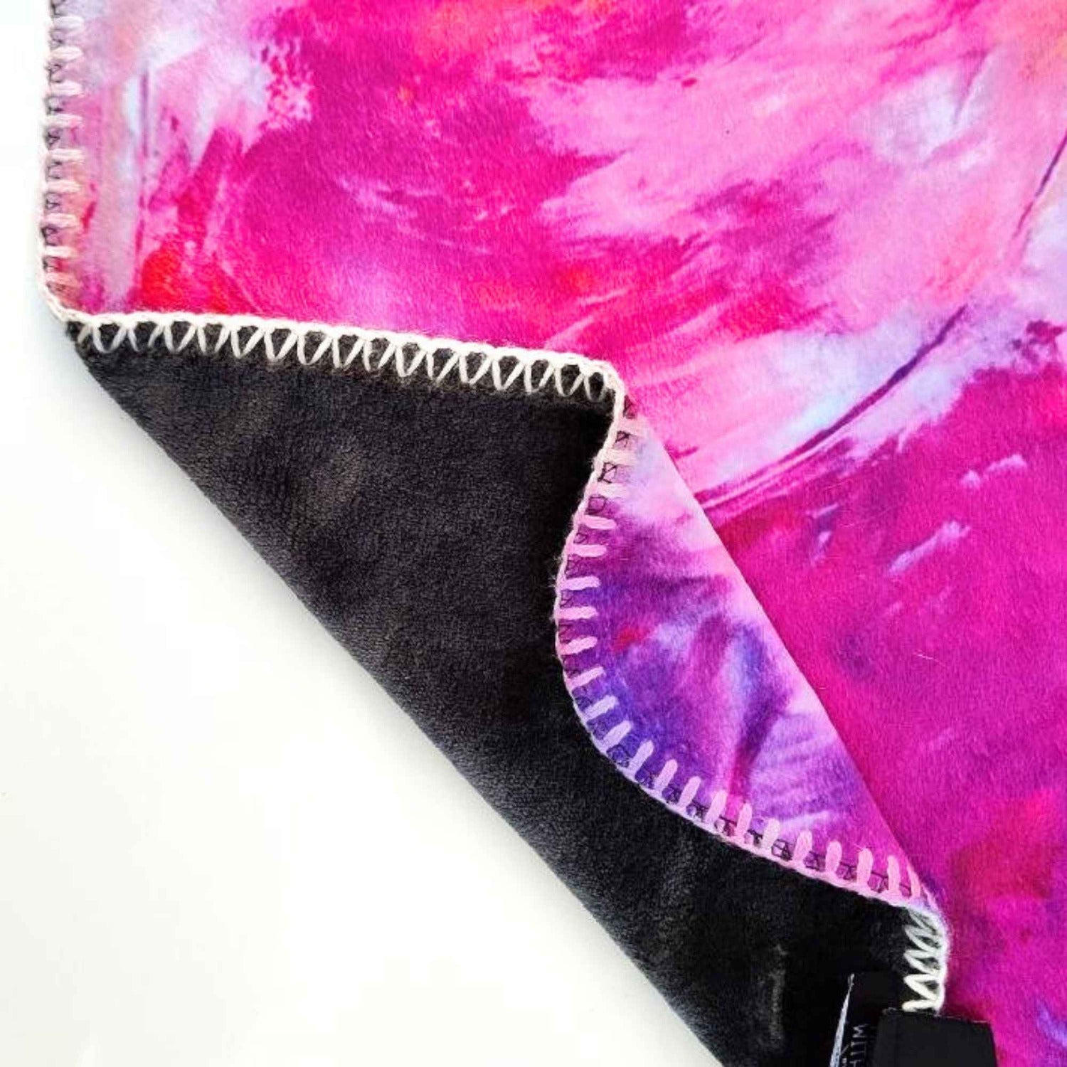Detail einer Kuscheldecke. Oberseite Pink mit weiß und rosa in abstraktem Muster, Unterseite anthrazit. Rand umstickt