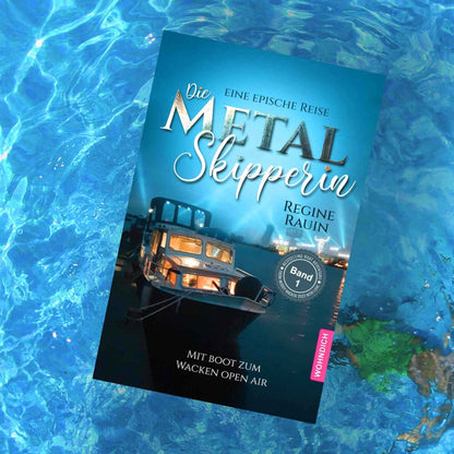 „Buch ‚Die Metal Skipperin – Band 1‘ auf Wasser, Cover mit beleuchtetem Boot bei Nacht und Festivallicht im Hintergrund.“