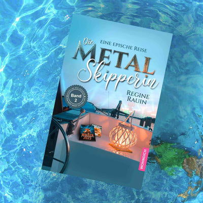 „Buch ‚Die Metal Skipperin – Band 2‘ auf Wasser, Cover mit Bootsszene, Lichtobjekt und Festivalbuch.“