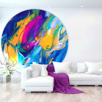 Runder, farbenfroher Teppich mit abstraktem Druck in Blau, Gelb, Pink und Grün vor einer weißen Sofalandschaft in modernem Wohnzimmer.