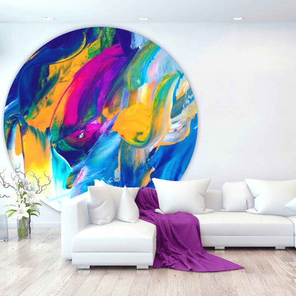 Runder, farbenfroher Teppich mit abstraktem Druck in Blau, Gelb, Pink und Grün vor einer weißen Sofalandschaft in modernem Wohnzimmer.